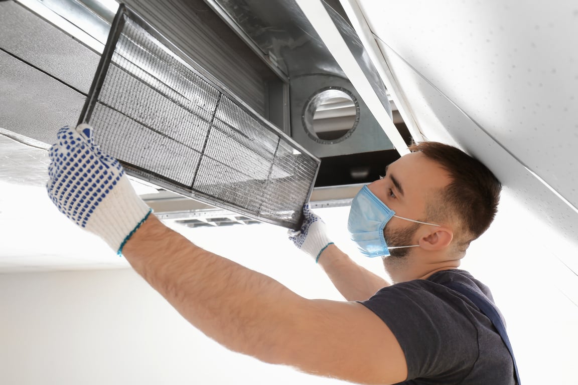 A Man Taking Down an Air Duct Filter